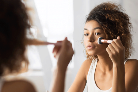 Woman looking in mirror while applying camouflage makeup